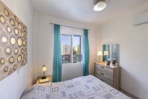 Une chambre à coucher comprenant un lit, une commode, une fenêtre avec des rideaux et un mur orné d’un motif géométrique.