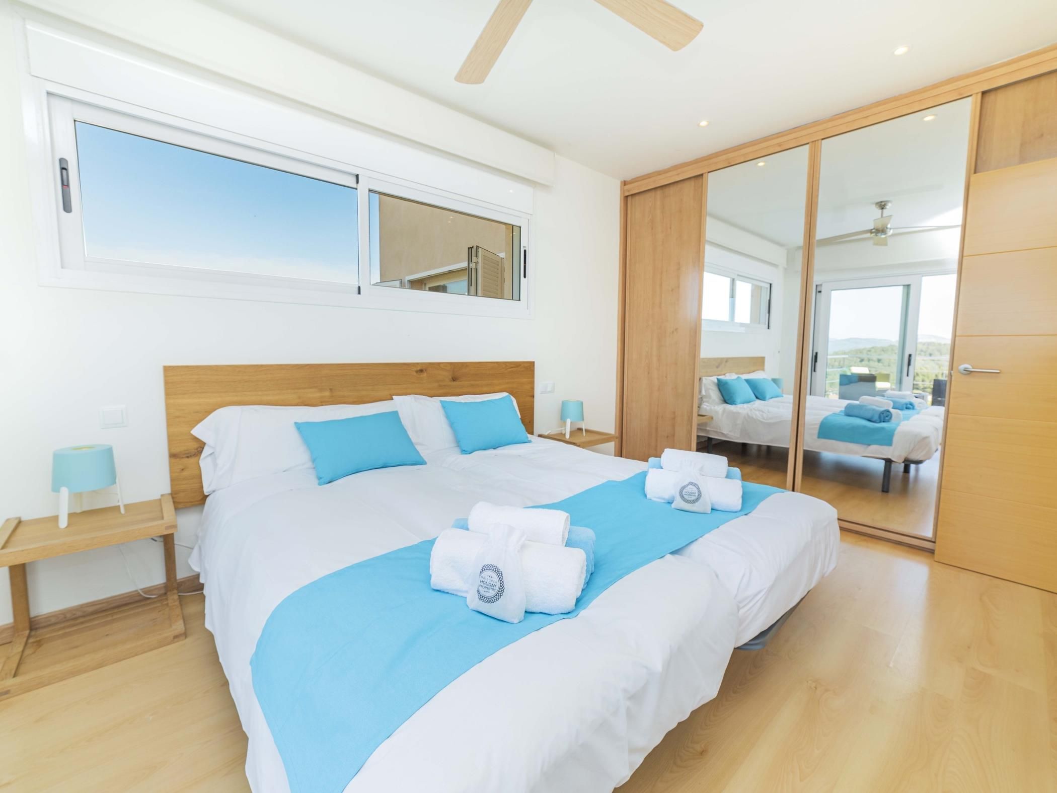 A modern bedroom with a large bed, a sliding door to a balcony, and a view of the outdoors.
