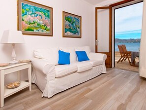 A white sofa with blue cushions, a white side table with a lamp, and two framed paintings on the wall.