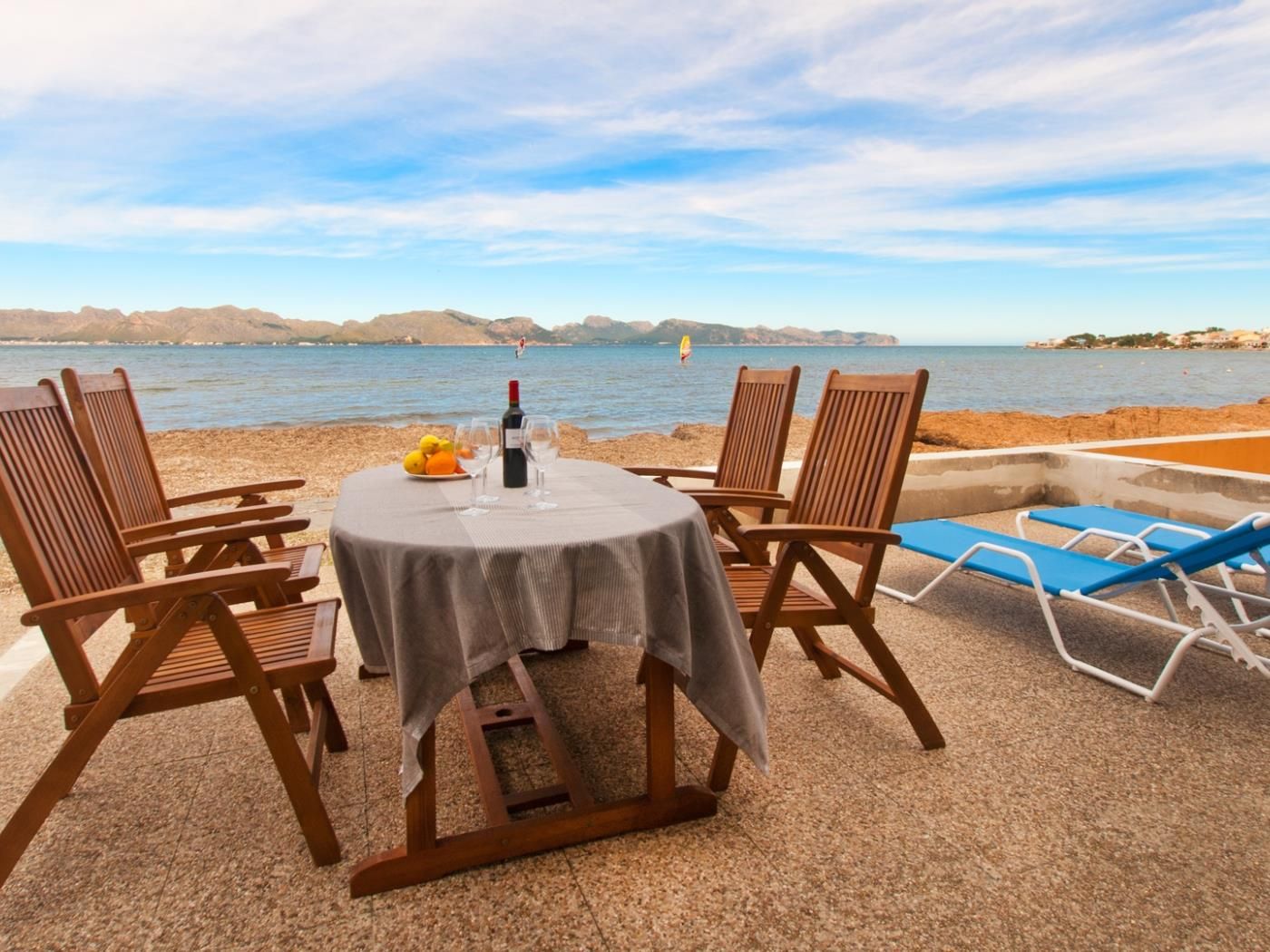 Une table dressée avec des chaises et une bouteille de vin, donnant sur une étendue d’eau avec des montagnes à l’horizon.