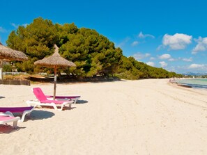 A beach with white sand, a row of pink and white lounge chairs, and a thatched umbrella.