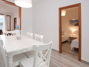 A dining area with a white table and chairs, a candle, and a view of a bedroom with a bed and a painting.