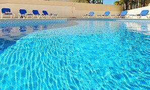 A clear swimming pool with blue water, surrounded by white lounge chairs with blue cushions.