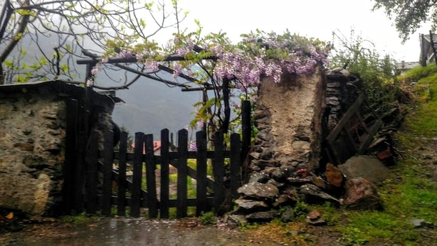 Un muro de piedra rústico con una verja de madera, una cerca de madera y otro muro de piedra.