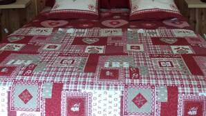 Una cama con un patrón rojo y blanco acolchado, cabecera de madera y almohadas con forma de corazón.