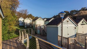 A row of small, light-colored cabins with wooden railings and a wooden deck in the foreground. - Ospreys - With a balcony and within a short walk of the beach (Bournemouth)