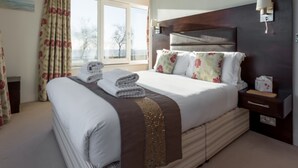 A neatly made bed with a headboard, a bedside table with a lamp, and a window with curtains. - Ospreys - With a balcony and within a short walk of the beach (Bournemouth)
