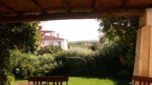 Une terrasse avec une table et un banc en bois, entourée d’une végétation luxuriante et offrant une vue sur un bâtiment situé au loin.