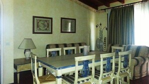Un coin repas avec une table et des chaises, des tableaux encadrés au mur, une lampe et une fenêtre avec des rideaux.