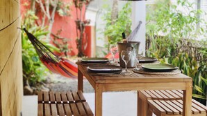 Una mesa de madera con una botella de champán, copas y platos, al aire libre.