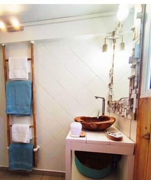 Ein Badezimmer mit einem Holz-Handtuchhalter, einem weißen Waschbecken mit einer Holzschale und einem Spiegel mit einer besonderen Leuchte.