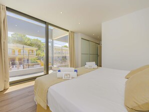 Ein Hotelzimmer mit einem großen Bett, Blick auf ein Gebäude mit Balkonen und einer Schiebetür.
