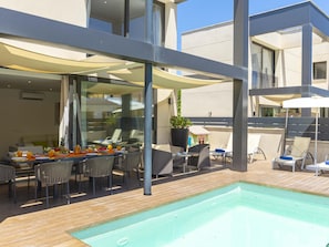 A modern outdoor pool area with a dining setup, lounge chairs, and a clear view of the building's architecture. - Villa Jade I· Villa with private pool in Can Picafort (Can Picafort)