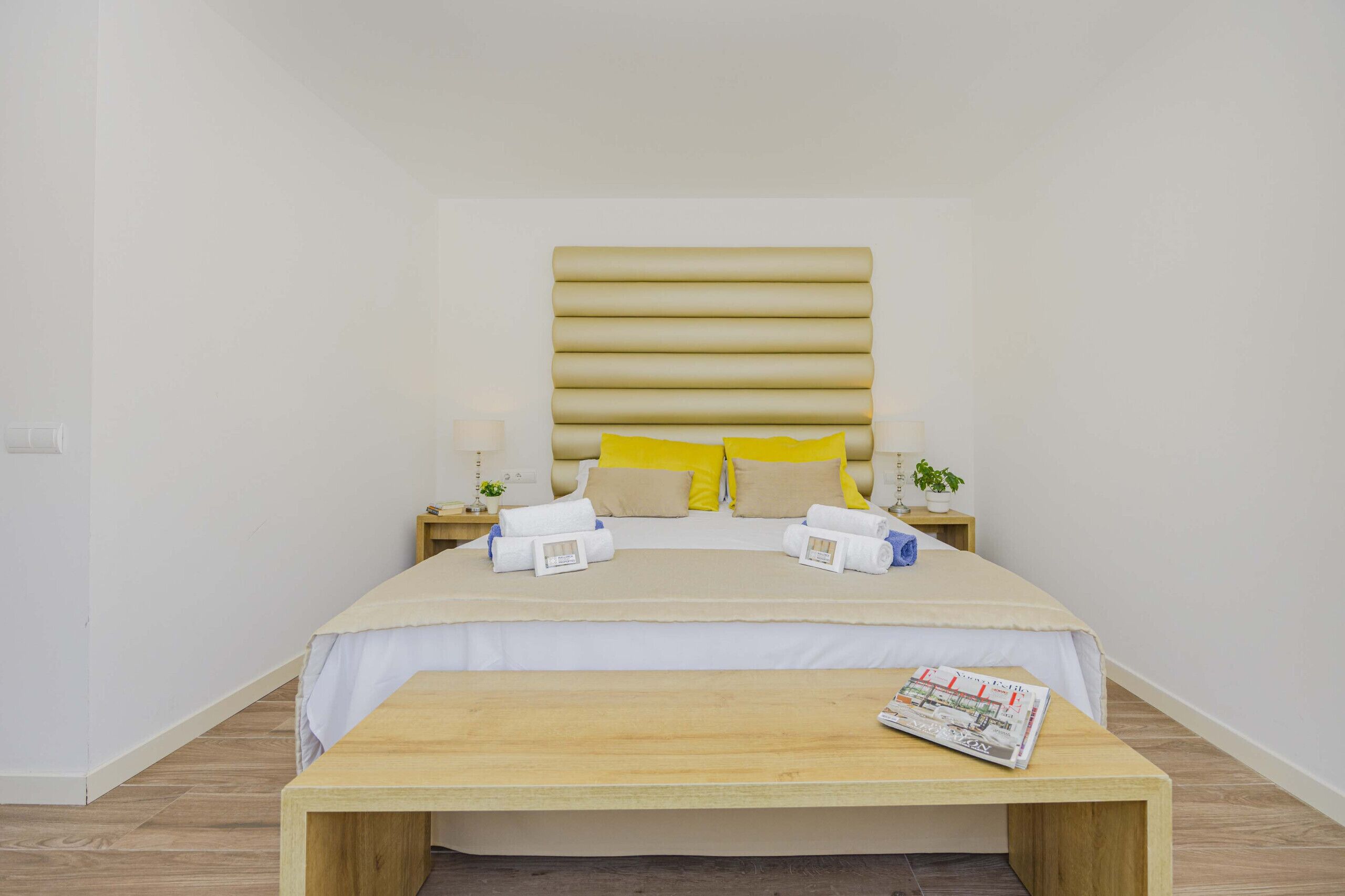A hotel room with a bed, bedside tables, a bedside lamp, a small plant, and a magazine on the bed.