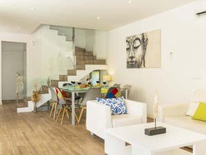 A modern living room with a dining area, a staircase, and a painting on the wall.