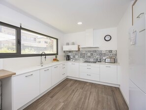 A modern kitchen with white cabinets, a wooden countertop, a built-in oven, and a window with a view of buildings outside. - Villa Jade I· Villa with private pool in Can Picafort (Can Picafort)