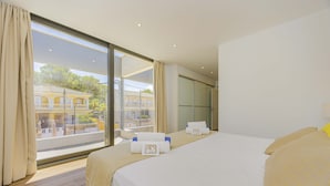 A hotel room with a large bed, a balcony with a view of buildings, and a sliding door to a private area. - Villa Jade I (Can Picafort)