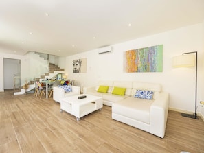 A modern living room with a white sofa, two white coffee tables, and a colorful abstract painting on the wall. - Villa Jade I· Villa with private pool in Can Picafort (Can Picafort)