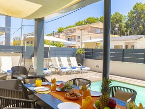 Ein Essbereich im Freien mit Blick auf den Pool, Liegestühlen und einem Tisch, der mit Speisen und Getränken gedeckt ist.