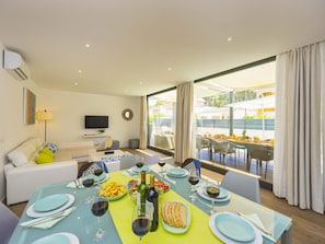 A modern living room with a dining area, a flat-screen TV, and a large window with a view of the outdoors. - Villa Jade I· Villa with private pool in Can Picafort (Can Picafort)