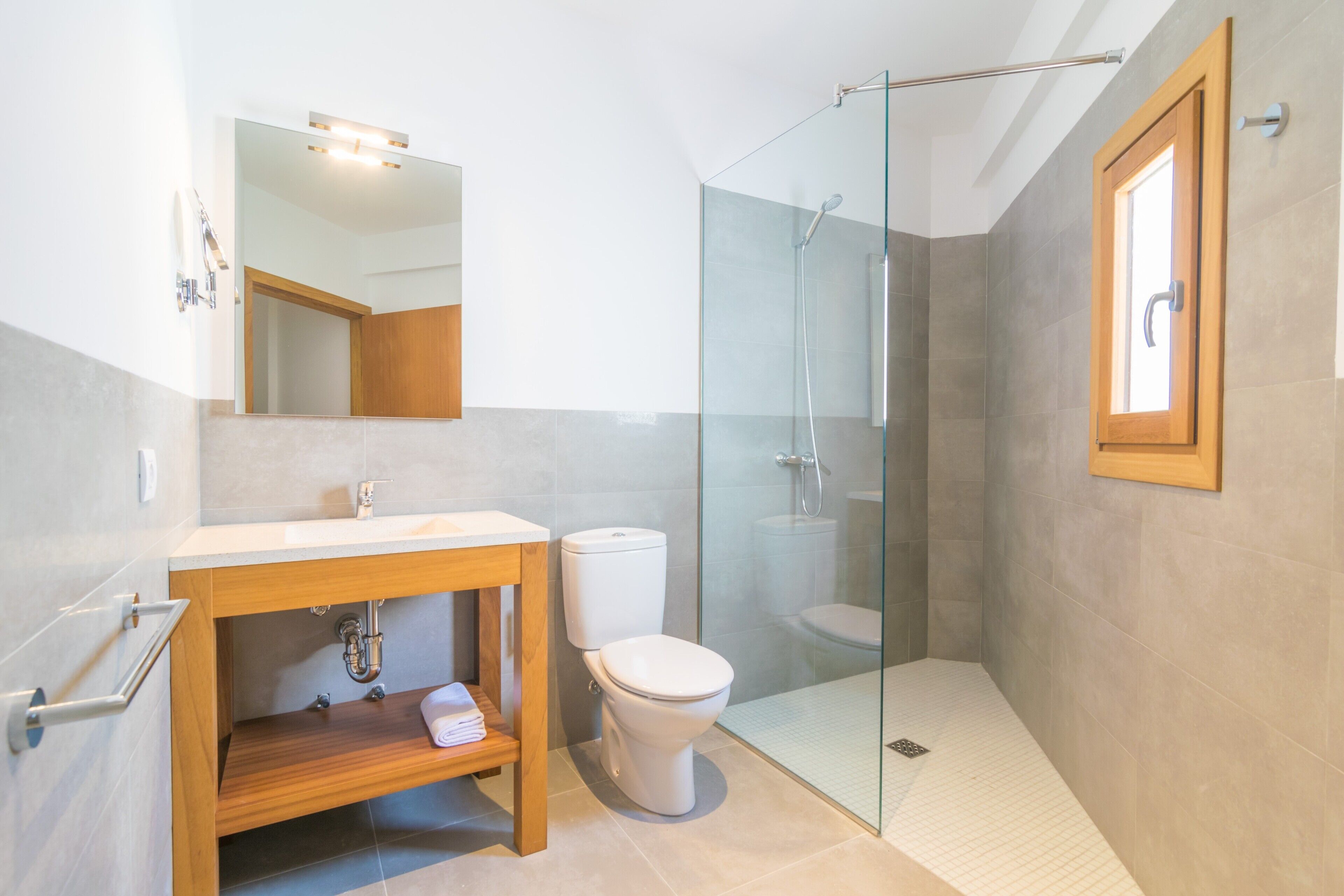 A modern bathroom with a glass-enclosed shower, a wooden vanity, and a toilet.