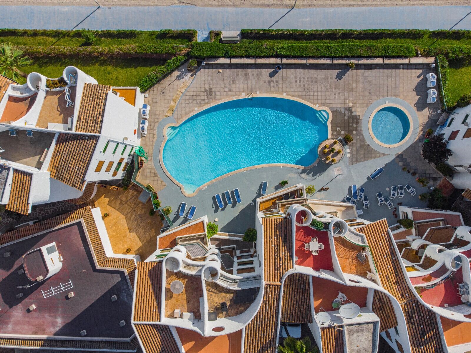 An aerial view of a resort with a central swimming pool, multiple lounge areas, and a variety of outdoor seating arrangements.