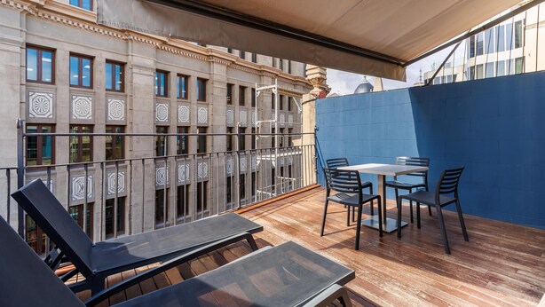 A balcony with a wooden floor, a table with chairs, and a blue wall. - Penthouse with private terrace in the heart of El Born (Barcelona)