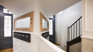 A hallway with a checkered floor, a staircase with a black railing, and two large ornate mirrors on the walls. - Penthouse with private terrace in the heart of El Born (Barcelona)