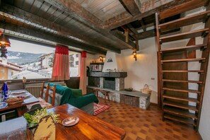 A rustic interior with a wooden table, a sofa, a fireplace, and a view of the outside.