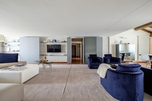 Ein modernes Wohnzimmer mit Sofa, Sesseln, Couchtisch und Fernseher.