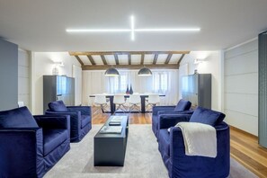 A modern living room with dark blue sofas, a central coffee table, and a dining area with a white table and chairs.