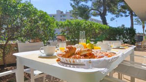 Une table dressée avec des croissants, du jus d’orange et un verre d’eau, avec en arrière-plan une vue sur des arbres et des bâtiments.