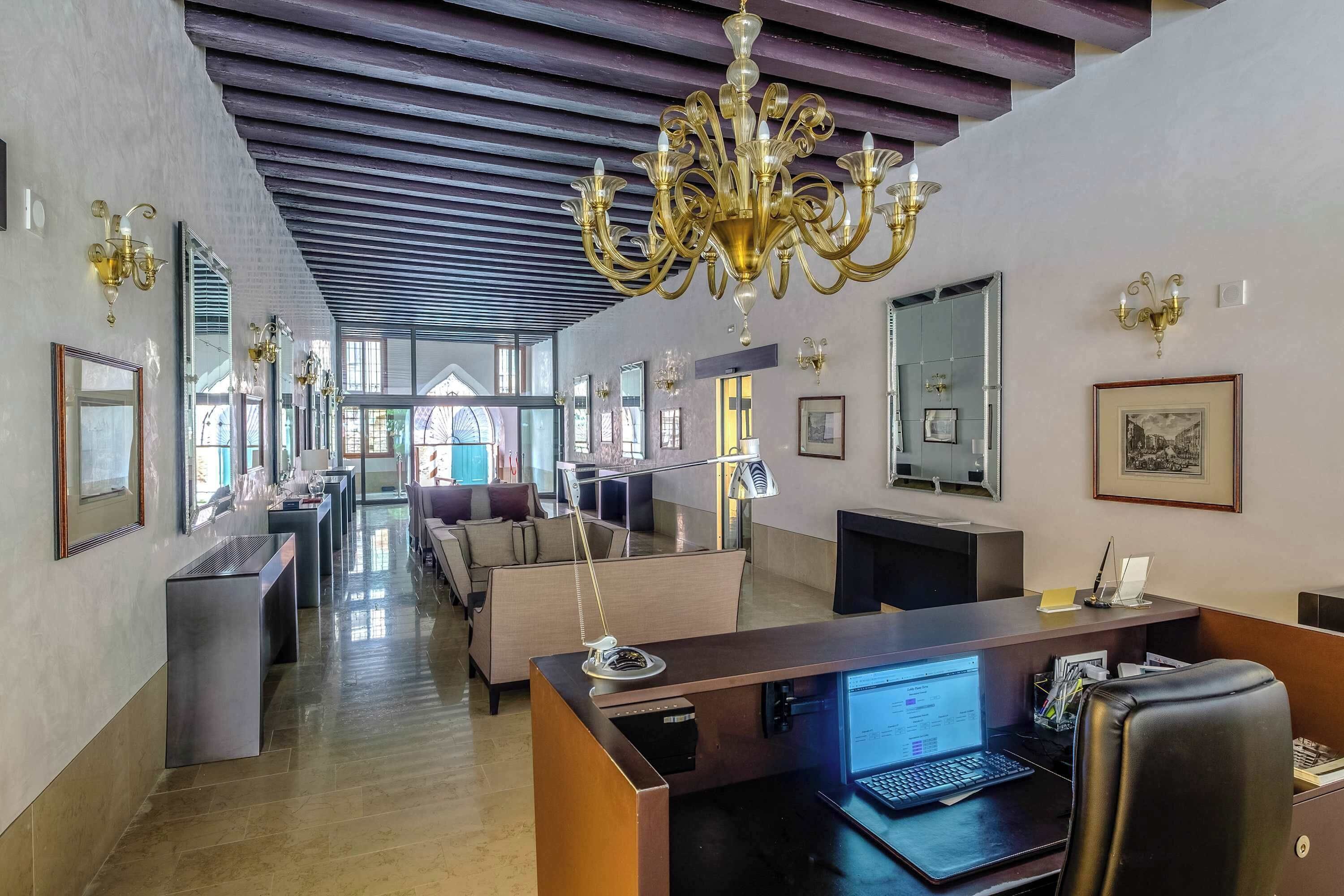 A modern hotel lobby with a reception desk, seating area, and a chandelier.