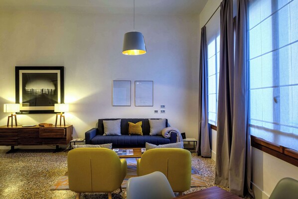 Una sala de estar moderna con un sofá, dos sillones, una mesita de centro, una lámpara y un cuadro en la pared.