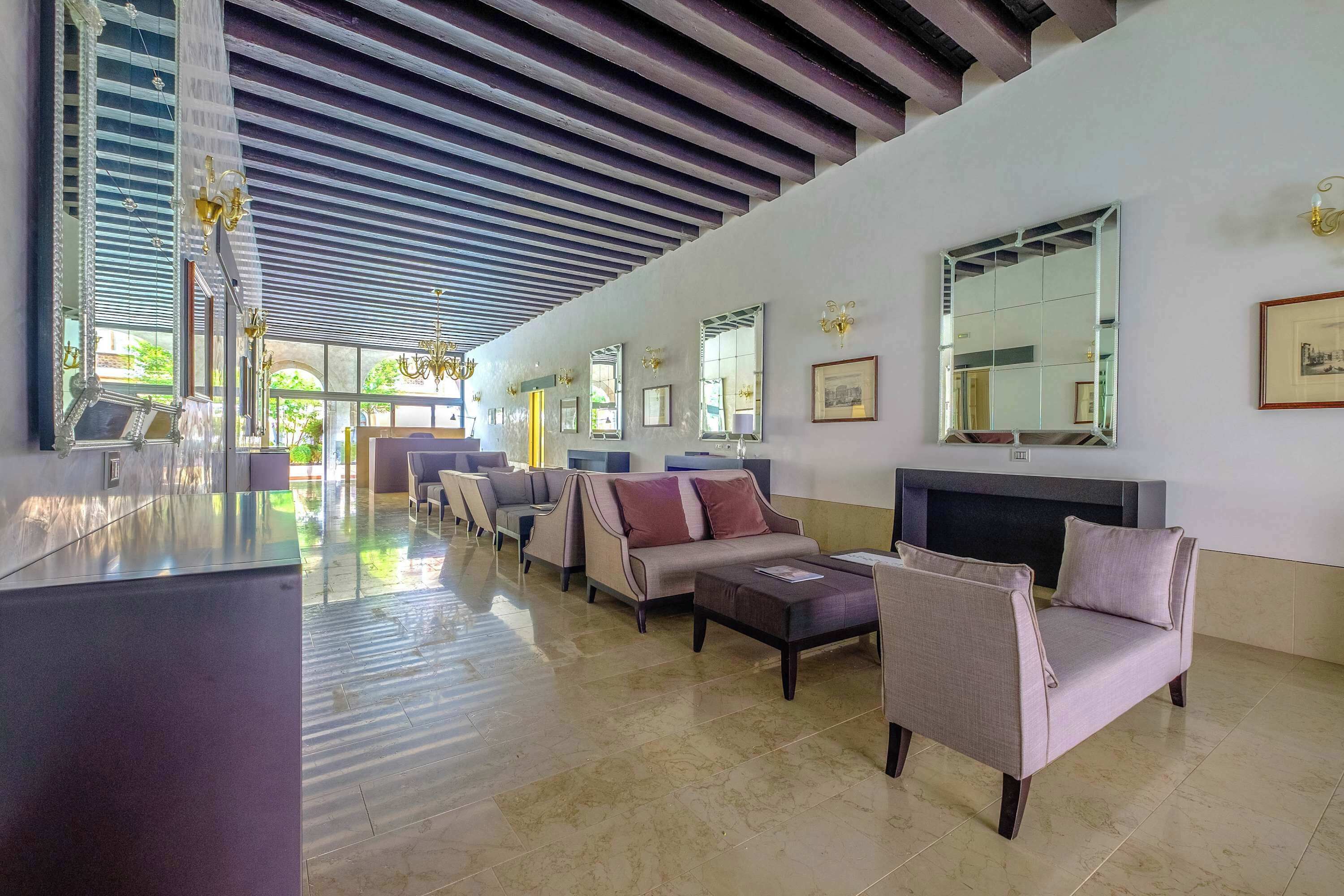 A spacious lobby with a high ceiling, multiple seating areas, and large mirrors on the walls.