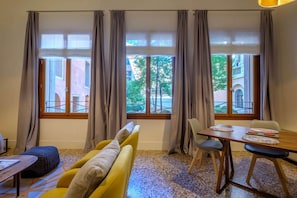 A room with a sofa, a dining table, and a window with curtains.