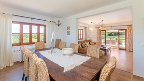 A dining area with a wooden table, woven chairs, and a view of the outdoors through large windows. - ANGIGAL - Spectacular villa with private pool in the tranquility of the countryside. Free (Manacor)