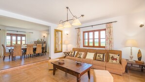 A spacious living room with a large sofa, dining table, and chairs. There is a mirror on the wall, a chandelier, and a window with curtains. - ANGIGAL - Spectacular villa with private pool in the tranquility of the countryside. Free (Manacor)