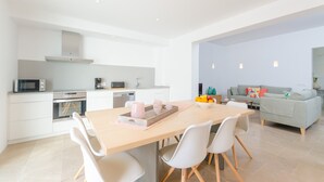 A modern kitchen with white cabinetry, a wooden dining table, and a grey sofa in the living area. - NA VALENTA - Villa with private pool in Artà. Free WiFi (Artà)