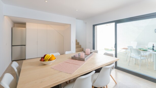 A modern dining area with a wooden table, white chairs, and a fruit bowl. - NA VALENTA - Villa with private pool in Artà. Free WiFi (Artà)
