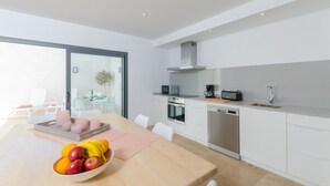 A modern kitchen with white cabinets, a built-in oven, microwave, and dishwasher. There is a dining area with a table set for two, and a large window providing natural light. - NA VALENTA - Villa with private pool in Artà. Free WiFi (Artà)