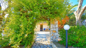 A stone pathway leading to a building with a door, surrounded by lush greenery and a white spherical light fixture. - Helona: Villa Estate, heated pool, stunning views, A/C (Kelia - Kassiopi)