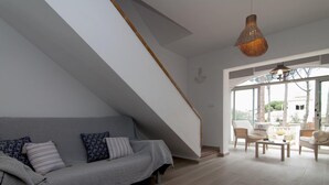 Una sala moderna con un sofá gris, una mesa de centro tejida y una escalera que conduce a un área exterior.