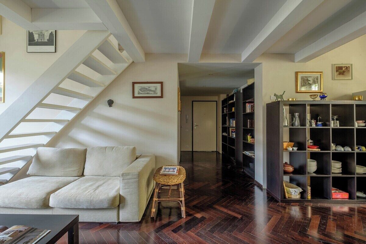 Una sala de estar con un sofá, un taburete, una estantería y una escalera.
