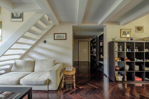 A living room with a sofa, a small stool, a bookshelf, and a staircase.