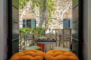An outdoor seating area with two cushioned chairs and a small table, surrounded by a brick wall and greenery.