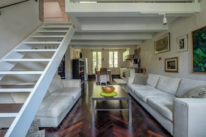 A modern living space with a staircase, a sofa set, a coffee table, and a kitchen area.