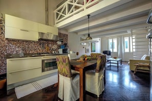 A modern kitchen with a dining area, featuring a high ceiling, a tiled backsplash, and a central island.