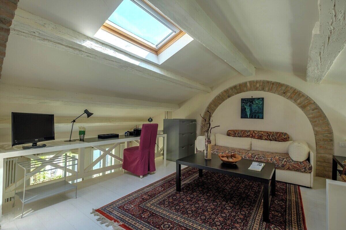 A room with a skylight, a sofa, a desk, and a television.