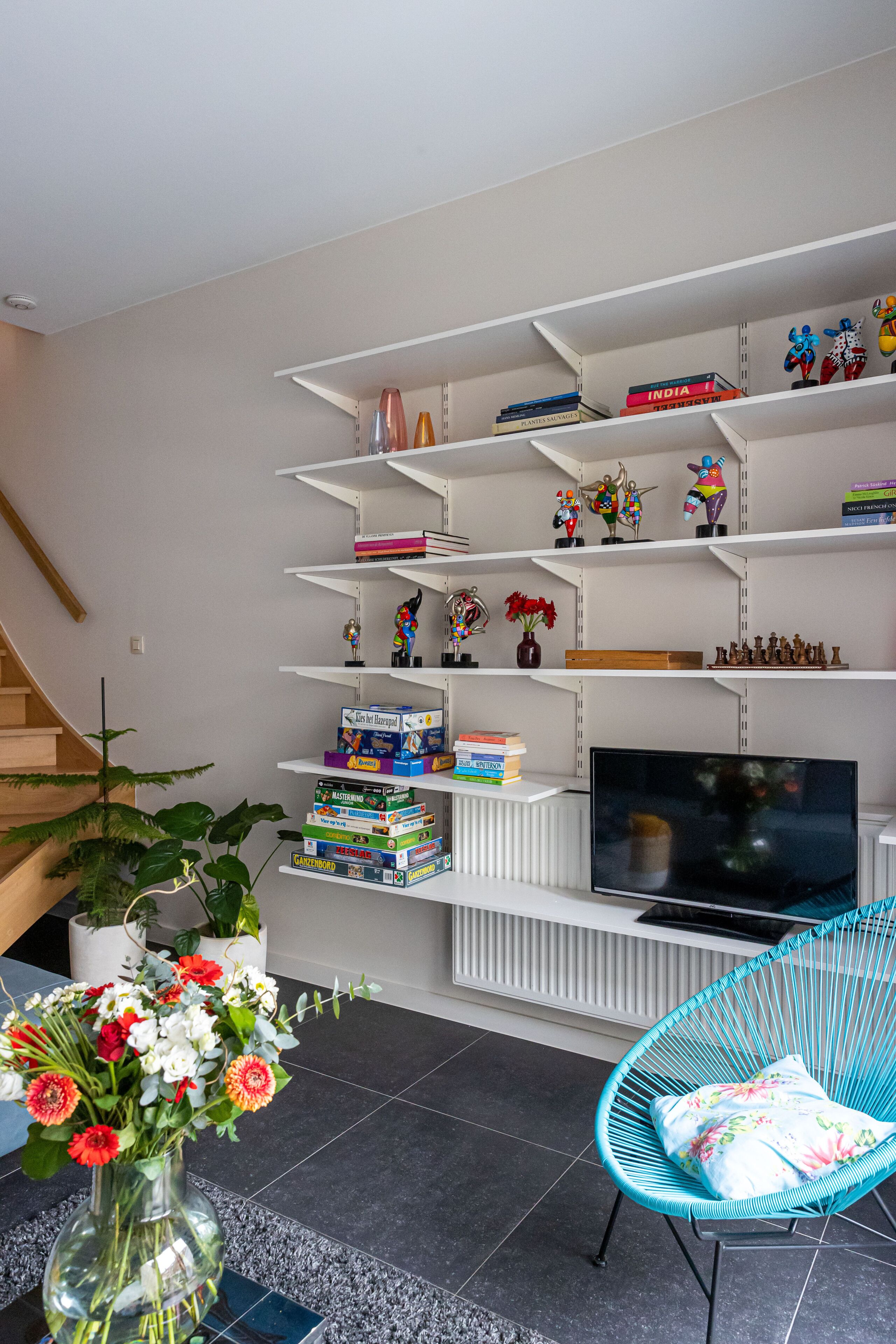 A living room with a TV, bookshelves, a blue chair, and a vase of flowers.